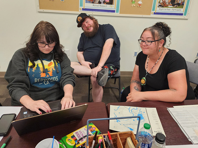 Two educator smiling and watching another work on the laptop on the table. 