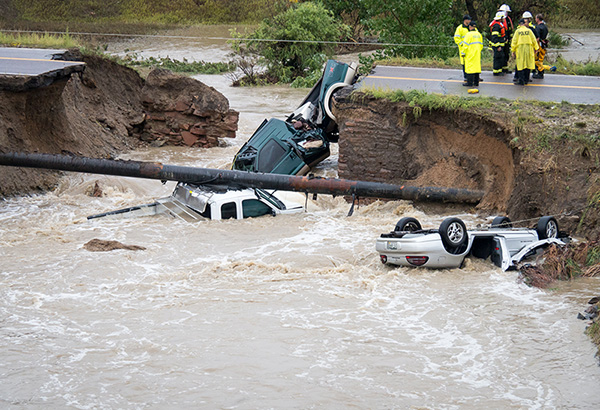 Photo of cars under water after a road to swept away during a flood with rescue crews in the background. 