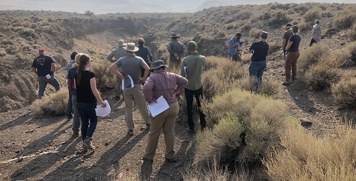 Researchers at a training course out in the shrub brush of the desert with mountains in distance.