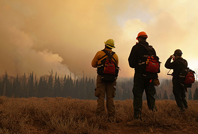 Researchers in hardhats watch as a wildfire burns in the distance.