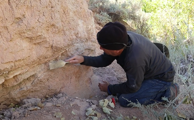 Archaeologist inspecting the side of a large rock formation.