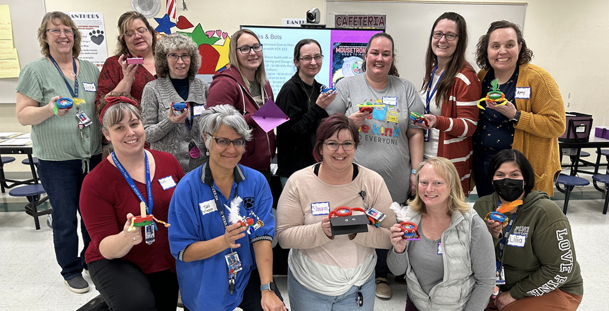 Teachers posing in a group with their robots created during a training event.