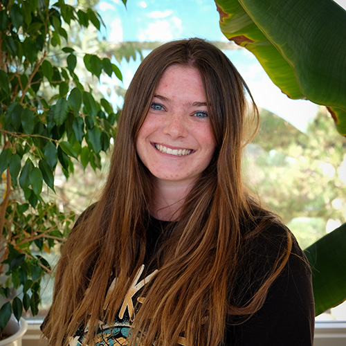 Photo of Olivia Hines with natural light with plants in the background. 