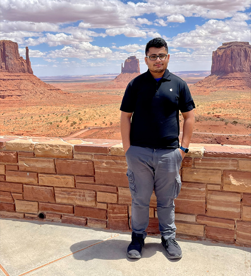 Photo of Monty in front of a red stone fence overlooking the red rocks of Monument Valley in Arizona. 