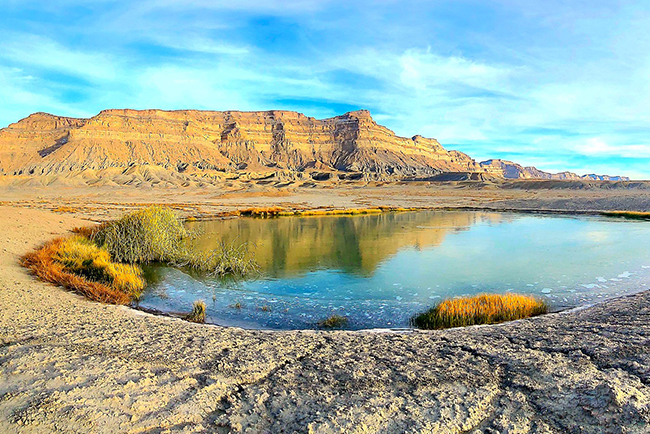 pool of water in the desert with mountains in the background and blue sky. 