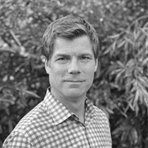 Black and White photo of Michael Wara in a checkered shirt in front of trees. 